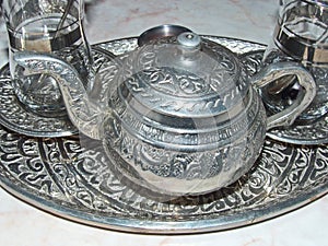 A shiny silver teapot and glasses on a tray. Traditional tea party in the Eastern style. Cooking battery.