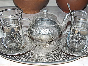 A shiny silver teapot and glasses on a tray. Traditional tea party in the Eastern style. Cooking battery.