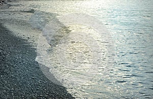 Shiny silver water on the sea pebble beach, early morning sunrise