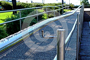 Shiny stainless steel guard and handrail along paved handicap ramp