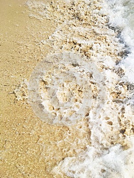 Shiny tropic sea wave on golden beach sand in sunset light.