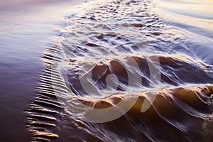 Shiny tropic sea wave on golden beach sand in sunset light