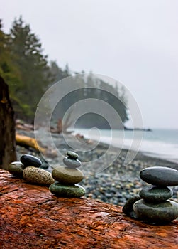 Shiny wet stone cairns piled on a fallen log on a rocky ocean beach.