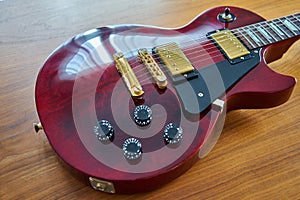 Shiny Wine Red Guitar With Golden Hardware on A Wooden Table Sid