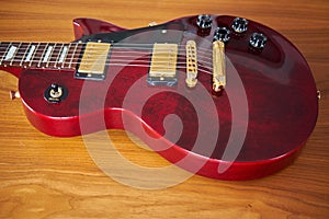 Shiny Wine Red Guitar With Golden Hardware on A Wooden Table Wit