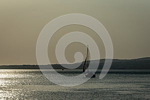 A ship on a background of a silver calm Black Sea at sunset. The sunny path on the water makes the landscape peaceful