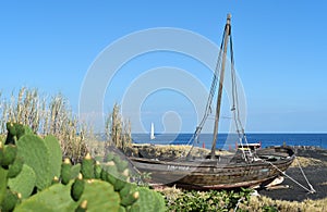 A ship on a black volcanic beach on the island of Stromboli, with a white sailing ship at sea in the background, Sicily, Italy
