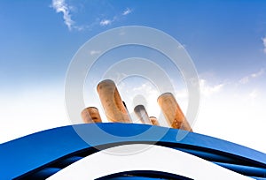 Ship exhaust funnel pipes and wavy blue cowling against blue clear sky with wispy white clouds.