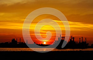 Ship and factory silhouetted at sunset