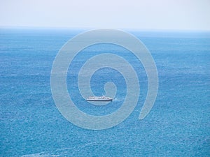 A ship in the middle of calm blue water and a clear sky on the horizon.