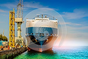 Ship moored alongside in shipyard near tower crane with rope, bow low angle on blue sky