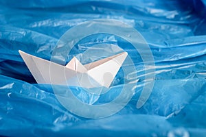 Ship origami of white paper among a blue plastic bag as if on waves of water. Conceptual photo