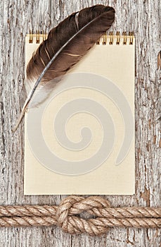 Ship rope, feather, spiral notebook and wood background