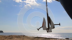 The ship`s anchor weighs in the air above the shore.