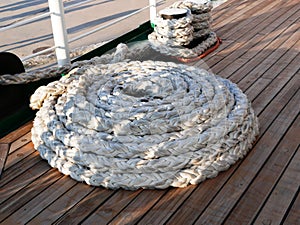 The ship`s rope is coiled in a spiral on the wooden deck of a sailing ship. Bay of white rope made of natural material on the deck