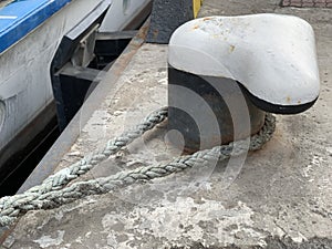 The ship`s rope is tied to a post in the dock. The ship is moored to the shore. The rope keeps the boat on the pier