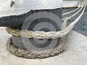 The ship`s rope is tied to a post in the dock. The ship is moored to the shore. The rope keeps the boat on the pier