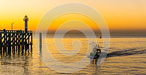 Ship sailing on the sea at the harbor of Blankenberge, Belgium, the pier with lighthouse, beautiful colorful sky at sunset