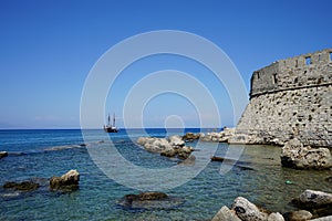 A ship with sails at sea at the walls of the Fort of Saint Nikolaos. Rhodes, Greece