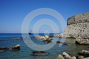 A ship with sails at sea at the walls of the Fort of Saint Nikolaos. Rhodes, Greece