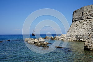 A ship with sails at sea at the walls of the Fort of Saint Nikolaos. Rhodes, Greece