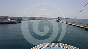 Ship sails smoothly over blue sea water at the harbor entrance towards pier