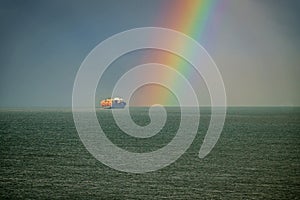 A ship at sea sails toward a rainbow.