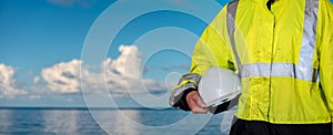 Ship supervisor engineer inspector stands at the dockside in a port. Wearing safety helmet and yellow vest. Cargo shipping