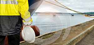 Ship supervisor engineer inspector stands at the dockside in a port. Wearing safety helmet and yellow vest. Cargo shipping