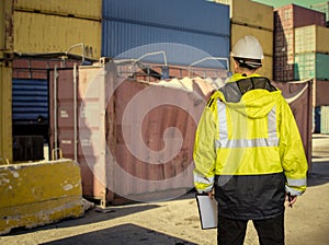 Ship supervisor engineer inspector stands at the dockside in a port. Wearing safety helmet and yellow vest. Cargo shipping
