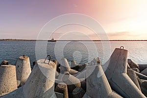 Ship-tugboat goes in high seas to tow cargo ship to port. Beautiful sunset over the pier. Tetrapod breAkwaters in harbor