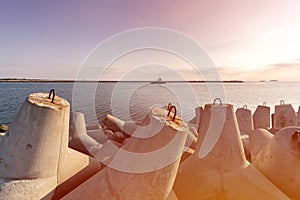 Ship-tugboat goes in high seas to tow cargo ship to port, Beautiful sunset over the pier, Tetrapod breakwaters in harbor