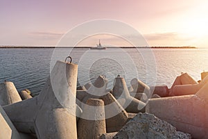 Ship-tugboat goes in high seas to tow cargo ship to port. Beautiful sunset over the pier. Tetrapod breakwaters in harbor