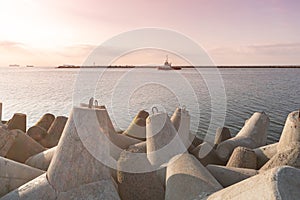 Ship-tugboat goes in high seas to tow cargo ship to port. Beautiful sunset over the pier. Tetrapod breakwaters in harbor