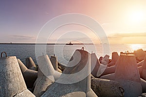 Ship-tugboat goes in high seas to tow cargo ship to port. Beautiful sunset over the pier. Tetrapod breakwaters in harbor