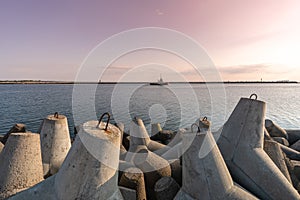 Ship-tugboat goes in high seas to tow cargo ship to port. Beautiful sunset over the pier. Tetrapod breakwaters in harbor