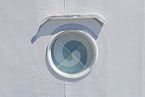 Ship window or porthole on white metall wall with cross.