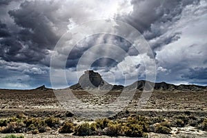 Shiprock view with gloomy and cloudy sky with sun rays shining through and brightening around