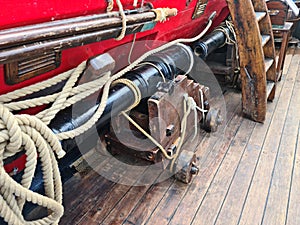 The ships cannon is secured with ropes on the deck of an old wooden sailboat