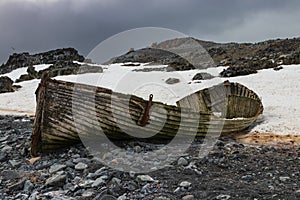 Shipwrecked boat on beach, Antarctic Island. Rocks and snow. Cloudy sky.