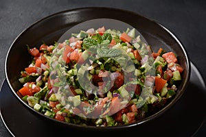 Shirazi Salad with tomatoes, cucumbers, red onions, parsley and mint with fresh lemon juice in a black bowl.
