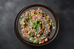 Shirazi Salad with tomatoes, cucumbers, red onions, parsley and mint with fresh lemon juice in a black bowl.