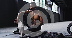 Shirtless african american man resting after battling ropes in an empty urban building