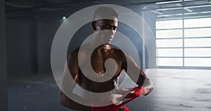 Shirtless african american man wrapping hands for boxing in an empty urban building