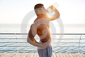 Shirtless african muscular young man drinking water on pier