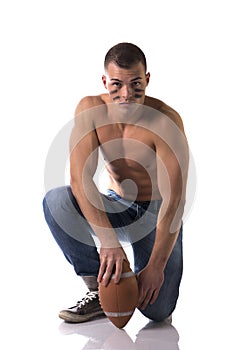 Shirtless american football player in jeans with ball kneeling