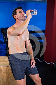 Shirtless athlete drinking water in gym