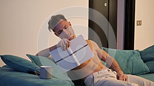 Shirtless athletic young man reading book on sofa