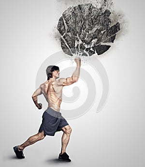 Shirtless athletick male kicking big grey rock.