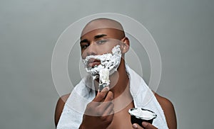 Shirtless attractive young african american man looking at camera, using brush while applying shaving foam on his face